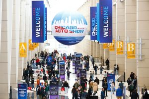2025-Chicago-Auto-Show-FEATURE: Banners and Large sphere with Show logo printed on it. Crowds of people under them walking to the show halls.