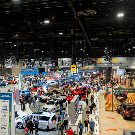 2026 Chicago Auto Show by the Numbers; Busy auto show with crowds exploring diverse car exhibits in a large convention center. Bright displays and vehicles create an energetic atmosphere.